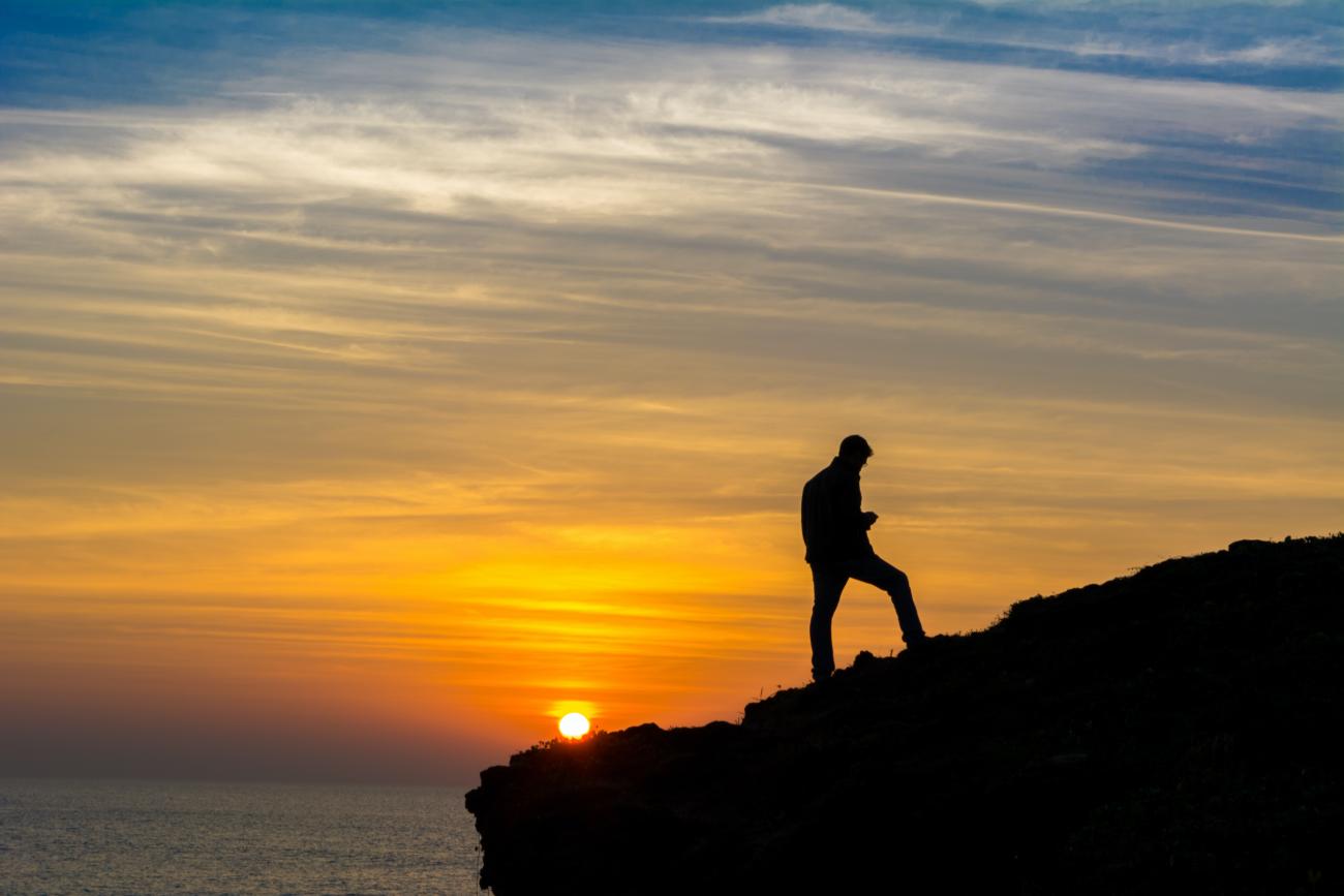 man standing on cliff with sunset in background